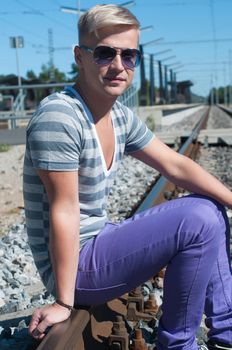 Young man in sunglasses sitting on the rail track