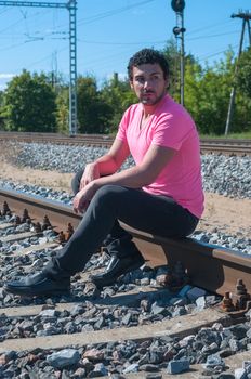 Young man in pink t-shirt sitting on the rail track