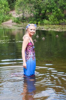 Beautiful blond woman in long dress standing in pond
