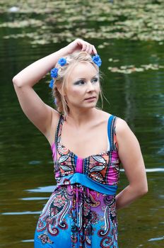 Beautiful blond woman in dress standing near the pond