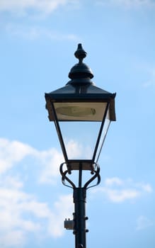 Black vertical old-fashioned lamppost against a blue sky