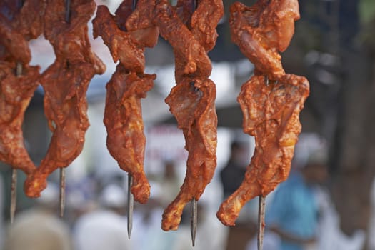 Chicken legs coated orange spices hanging from a street stall in Delhi, India