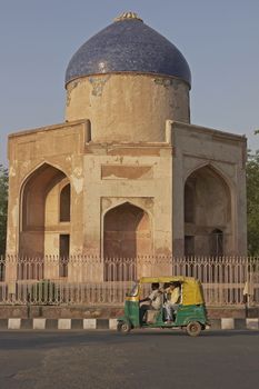 Auto rickshaw carrying passengers passing an Islamic Tomb in New Delhi, India