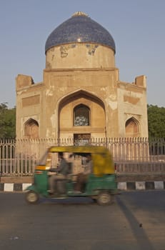 Auto rickshaw carrying passengers passing an Islamic Tomb in New Delhi, India