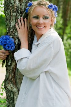 Beautiful smiling young woman in white shirt standing near the tree