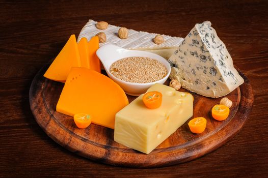 various cheeses with nuts and fruits on wooden plate