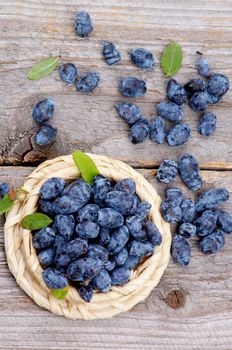 Fresh Ripe Honeysuckle Berries in Wicker Bowl on Rustic Wooden background. Top View