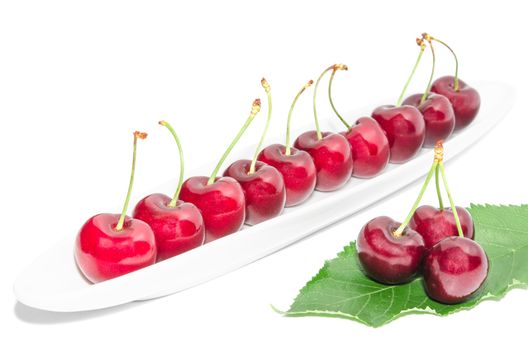 Big dark red ripe cherry berry row arranged on long white dish and fresh green leaf isolated