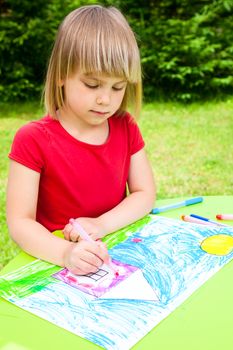 Little girl sitting at table drawing a house outdoors