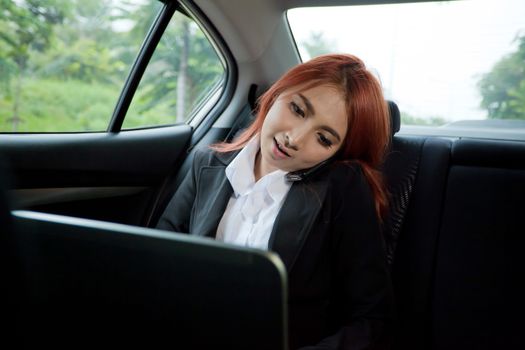 Beautiful young business asian woman using laptop and mobile phone in a car