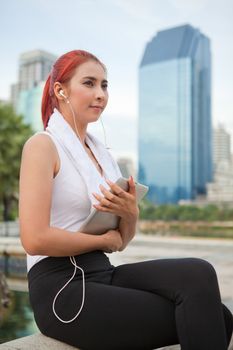 beautiful fitness asian woman listening to music with tablet in park city