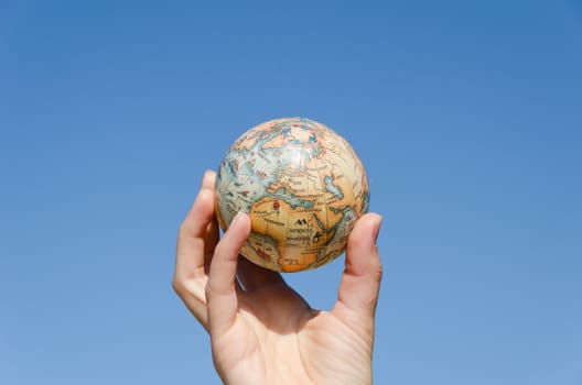 stylized global earth miniature in hand on blue sky background, environment control concept
