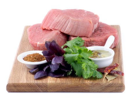 Wooden Cutting Board with Three Raw Beef Steaks, Greens, Spices and Olive Oil isolated on white background