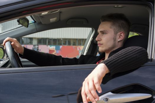 Handsome blond young man sitting in his car, looking in front of him 