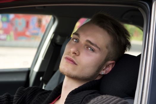 Handsome blond young man sitting in his car, looking at camera