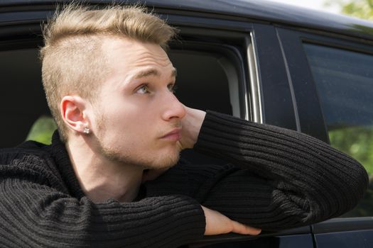 Handsome blond young man sitting in his car, looking out