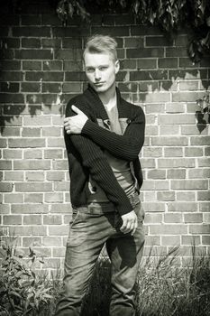 Handsome blond young man standing outside in front of brick wall looking at camera