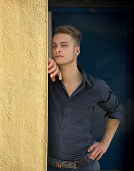 Attractive young blond man leaning against wall, looking at camera