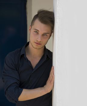 Attractive young blond man leaning against wall, looking at camera