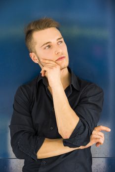 Attractive young man thinking, looking up with hand on his chin on blue background