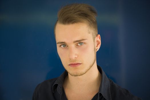 Headshot of attractive blond, blue eyed young man on blue background