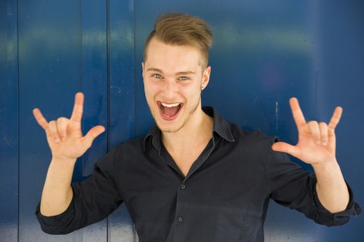 Happy handsome young man screaming and doing I Love You hand sign
