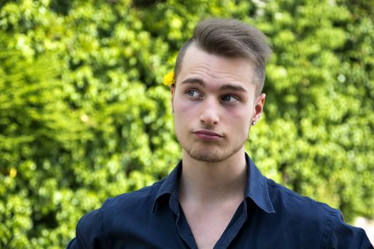 Attractive young man with unsure expression, thinking. Outdoors shot