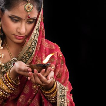 Beautiful Indian woman hands holding diya oil lamp, celebrating diwali festive of lights, traditional sari prayer isolated on black background with copy space on side.