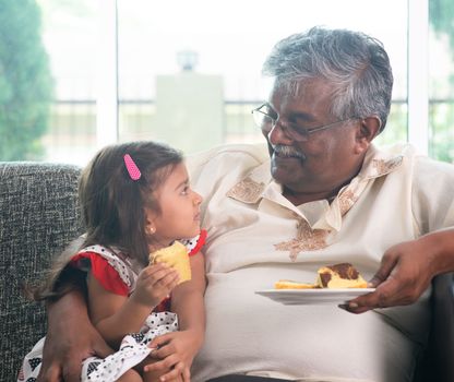 Portrait Indian family at home. Grandparent and grandchild eating cake. Asian people living lifestyle. Grandfather and granddaughter.