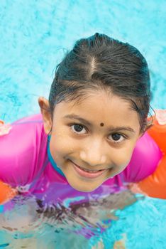 Asian kid in swimmer class with float bands. Indian child learning swimming in pool.