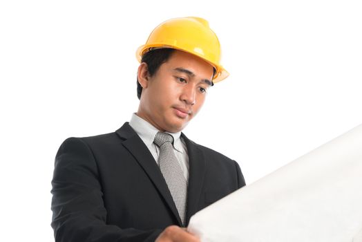 Close-up of an Asian young man wearing a hardhat looking at blueprint paper, standing isolated on white background.