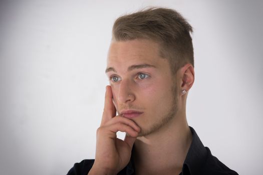 Attractive young man thinking, looking away with hand on his chin, on light background