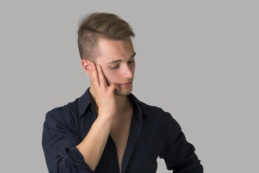 Sad, depressed blond young man looking down. Light grey background