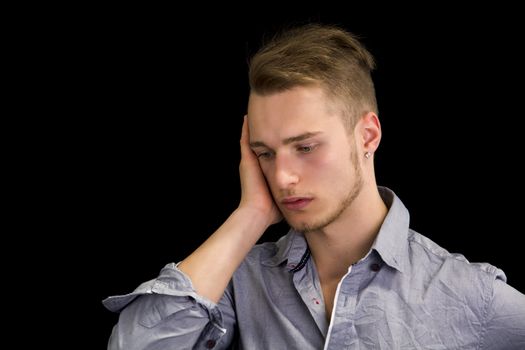 Sad or worried handsome young man looking down, isolated on black