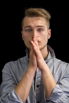 Attractive blond young man, serious expression with hands joined in front of mouth