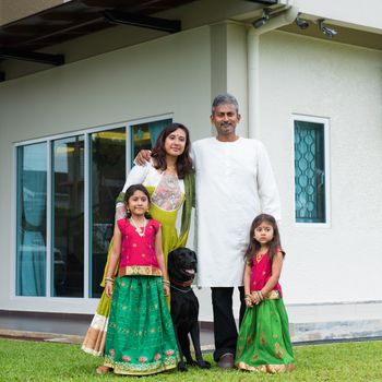 Beautiful Asian Indian family portrait smiling and standing outside their new house with pet dog.