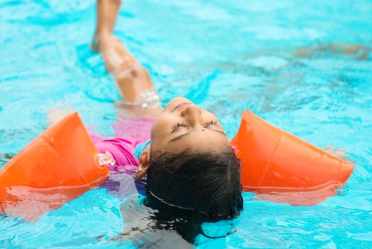 Indian child learning swimming in pool. Asian kid in swimmer class with float bands.