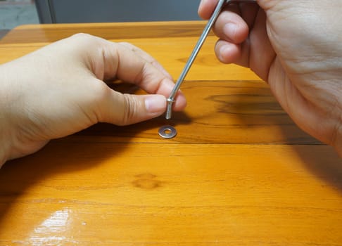 Woman using a screwdriver to tighten the screws on the wooden table.                               