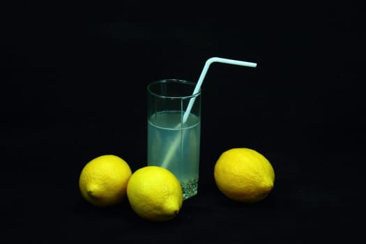 On a black background lemons and lemonade with straws