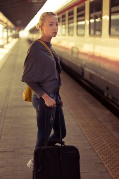 Blonde caucasian woman waiting at the railway station with a suitcase.