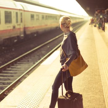 Blonde caucasian woman waiting at the railway station with a suitcase.