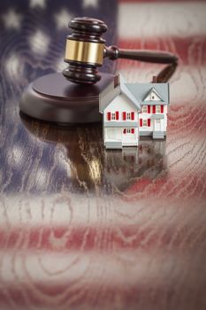 Small House and Gavel on Wooden Table with American Flag Reflection.