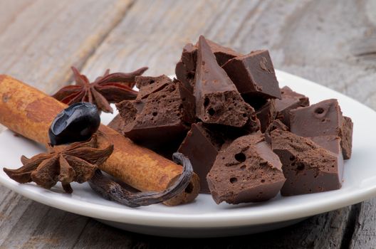 Arrangement of Dark Chocolate Pieces with Vanilla Pod, Anise Stars and Cinnamon Stick on White Plate closeup on Wooden background