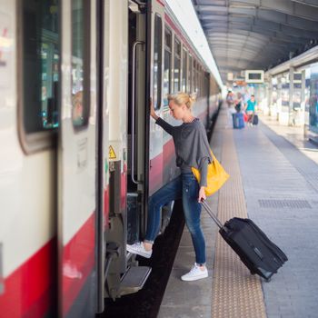 Blonde caucasian woman waiting at the railway station with a suitcase.