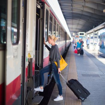 Blonde caucasian woman waiting at the railway station with a suitcase.