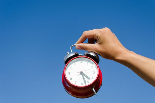 female hand hold red chrome shiny alarmclock on blue sky abckground