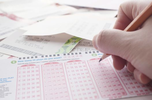 Close-up of a person marking number on lottery ticket with lottery ticket background