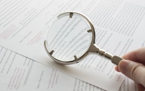 Close up hand holding magnifying glass to read document