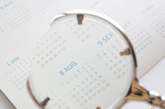Hand holding magnifying glass to checking calendar of August