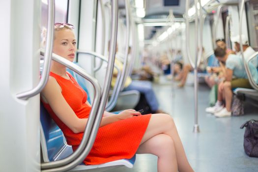 Beautiful blonde caucasian lady in red dress traveling by metro.